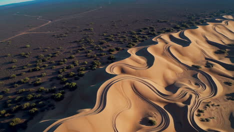 aerial view of desert sand dunes with wavy patterns and tire tracks