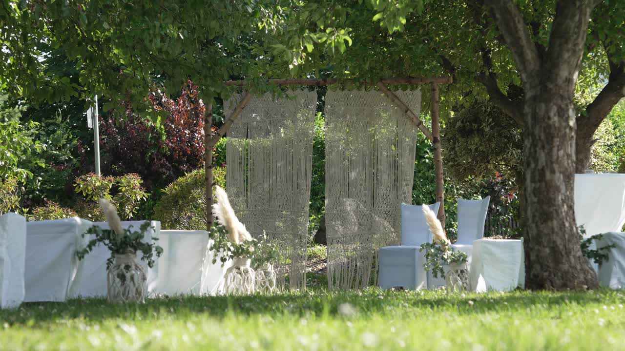 Location per cerimonia di matrimonio all'aperto con arco decorato, sedie bianche e composizioni floreali in un ambiente da giardino