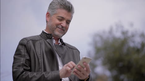 hombre maduro sonriente usando un teléfono inteligente al aire libre