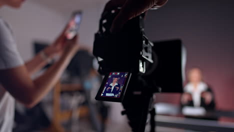 male hand touches a camera which display shows the female reporter. close up. unrecognized person taking video on the smartphone at blurred backdrop.