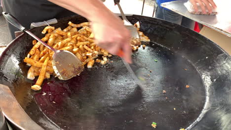 4k footage of a vendor with no face shown while cooking and stir frying a turnip cake on a flat large wok and metal ladles