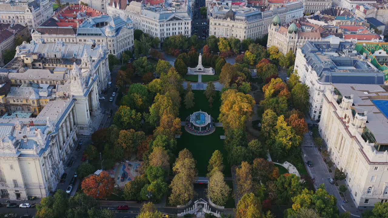 Aerial view of Szabadság Square in central Budapest, framed by historic buildings and autumn trees, with the Parliament and Danube in the distance