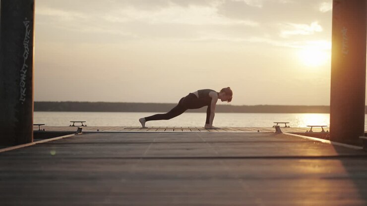 Giovane donna che fa yoga in una profonda posizione di allungamento su un pontile al tramonto