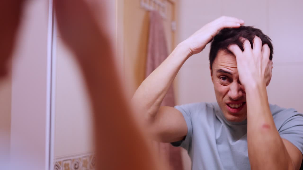 Insecure man combing hair before a date in bathroom mirror