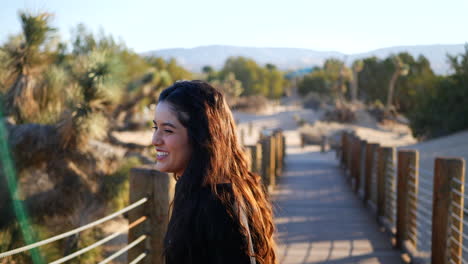 Una-Hermosa-Modelo-Sonriendo-Y-Riendo-Fuerte-Mientras-Intenta-Componerse-Para-Una-Sesión-De-Fotos-En-El-Desierto-Con-árboles-De-Joshua-En-Cámara-Lenta