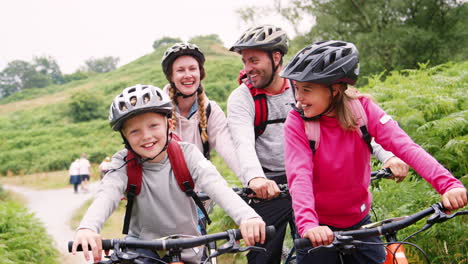 Parents-and-children-sitting-on-mountain-bikes-during-family-camping-trip,-close-up,-Lake-District,-UK