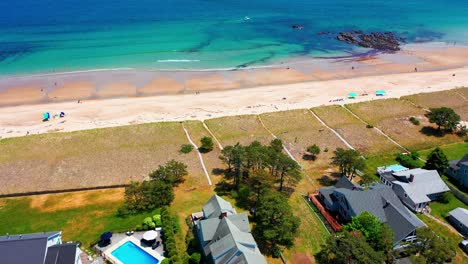 aerial drone footage above saco, maine beaches in summer. people relax under sun, kids run by waves, vacation houses overlook a packed shoreline. east coast coastal getaway at its peak
