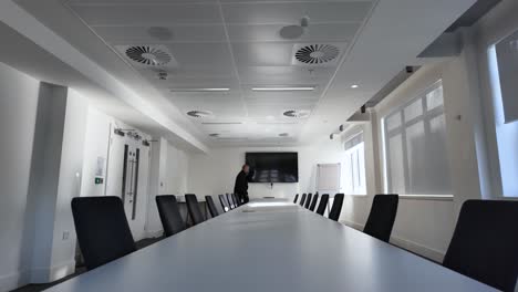 businessman walking alongside a long conference table in a spacious, modern meeting room, reflecting a professional corporate atmosphere