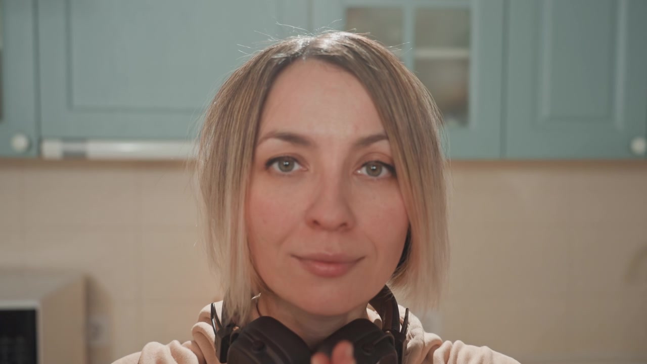 Kaukasische Frau in der Küche hört Musik, Kopfhörer um den Hals, führt ein meditatives Morgenritual mit erhobenen Armen durch, Nahaufnahme zeigt ruhigen Blick und leichtes Lächeln, weiches warmes Licht.