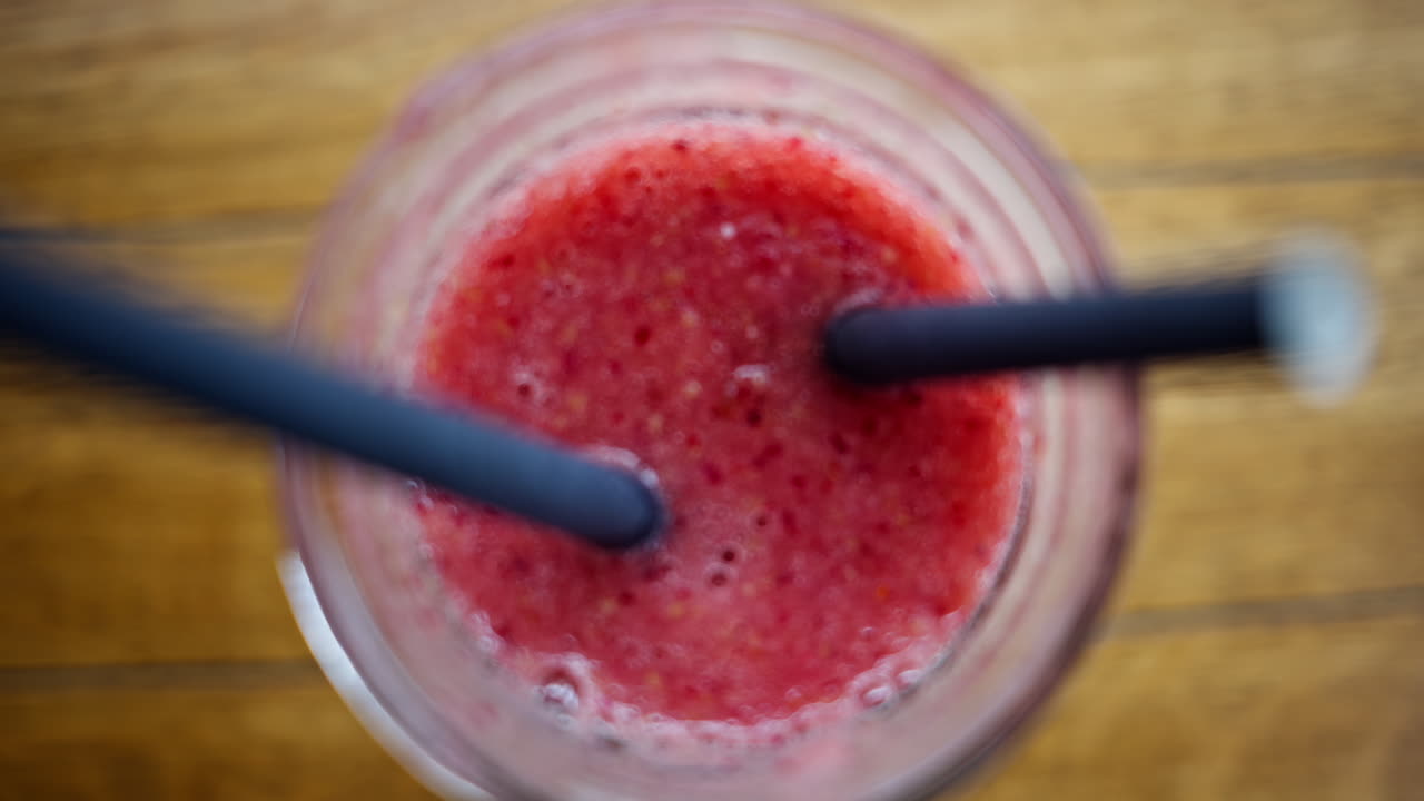 Primo piano di un bicchiere con un frullato rosso e due cannucce nere, su un tavolo