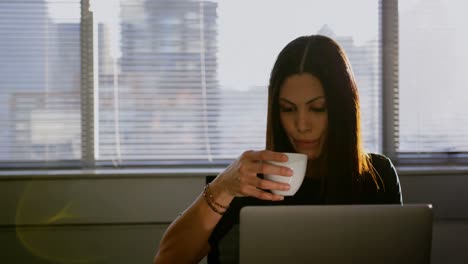 Front-view-of-young-Caucasian-businesswoman-drinking-coffee-while-working-on-laptop-in-office-4k