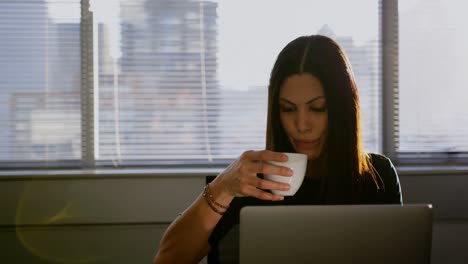 front view of young caucasian businesswoman drinking coffee while working on laptop in office 4k