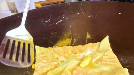 close-up of a golden pastry being fried and flipped on a hot griddle using a spatula.