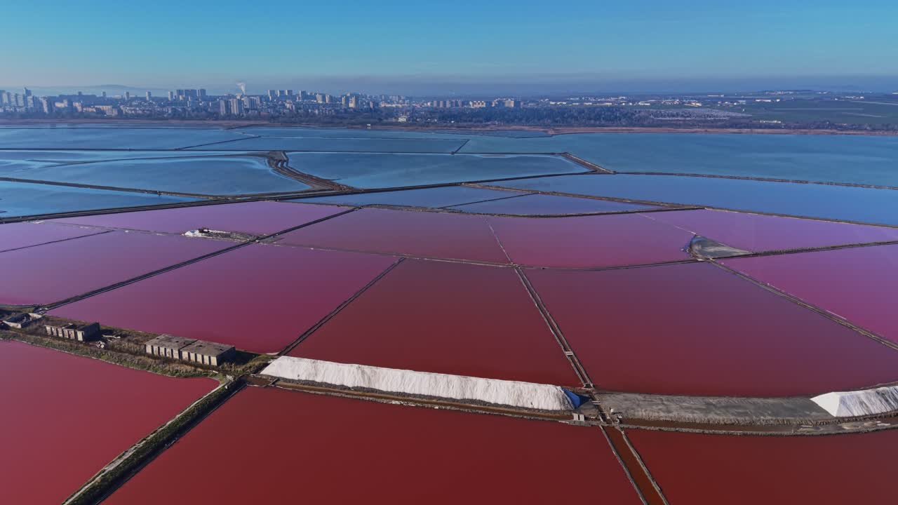 Salt production in large salt pans with city skyline in the background