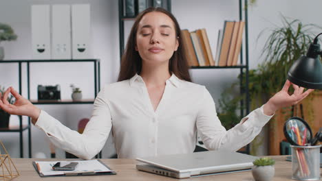 businesswoman working on laptop meditating doing yoga breathing exercise in lotus position at office
