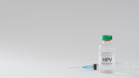 Video-close-up-of-hpv-vaccine-vial-and-syringe,-on-grey-background-with-copy-space