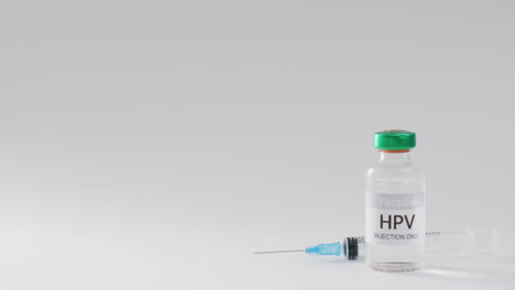 video close up of hpv vaccine vial and syringe, on grey background with copy space