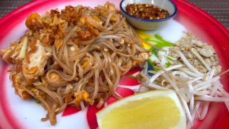 Spicy-Pad-Thai-noodles-dish-with-chicken,-crispy-onion,-bean-sprouts,-peanuts-and-chili-flakes-at-a-Thai-restaurant,-tasty-traditional-asian-food,-4K-shot
