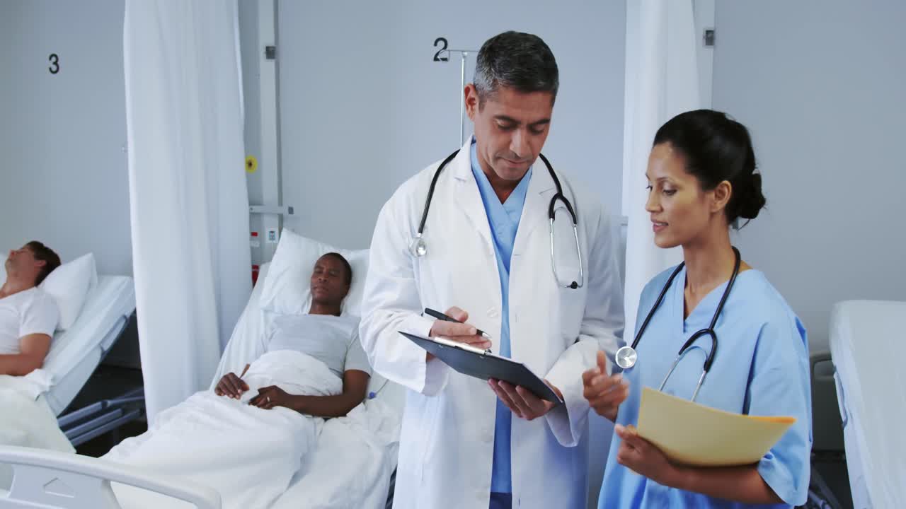 Front view of multi-ethnic doctors discussing over clipboard in ward at hospital