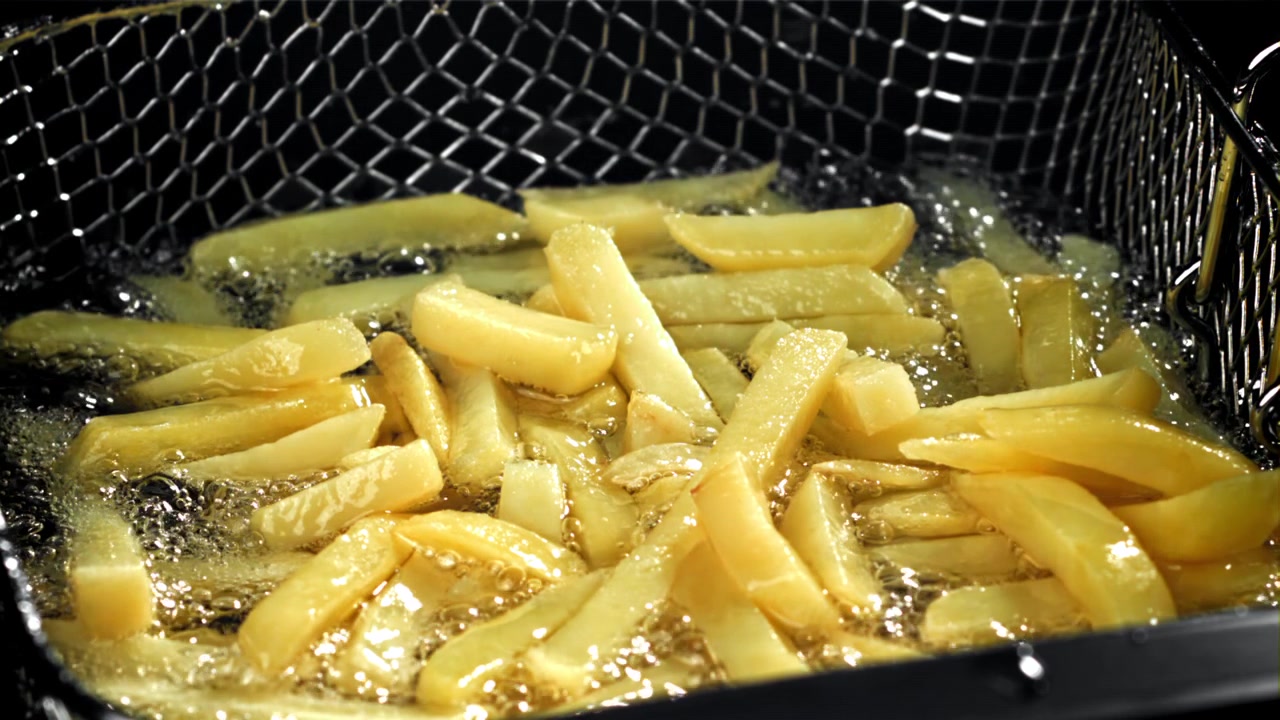 Patatas fritas friéndose en aceite caliente en una cesta de freidora