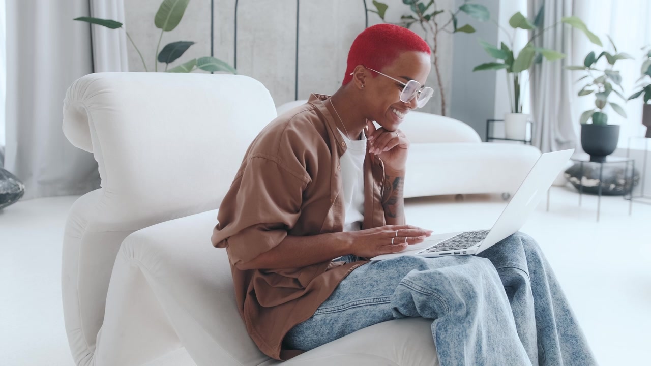 Young busy african american woman works with laptop sits in living room