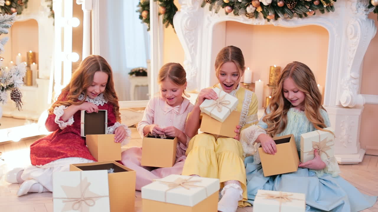 Four beautiful girls sitting at the fireplace open Christmas presents. Teenage kids rejoicing gifts.