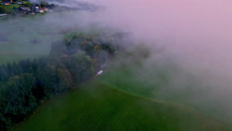 aerial drone top down shot over green agricultural fields through white clouds with the view of village houses in the background on a cloudy day