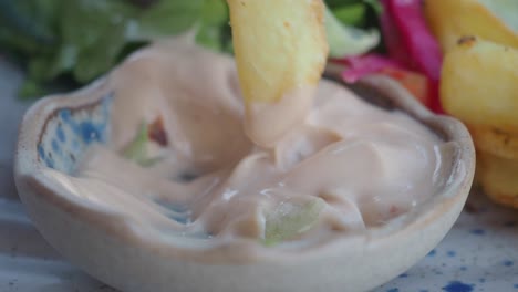 close up of a french fry being dipped in a creamy sauce