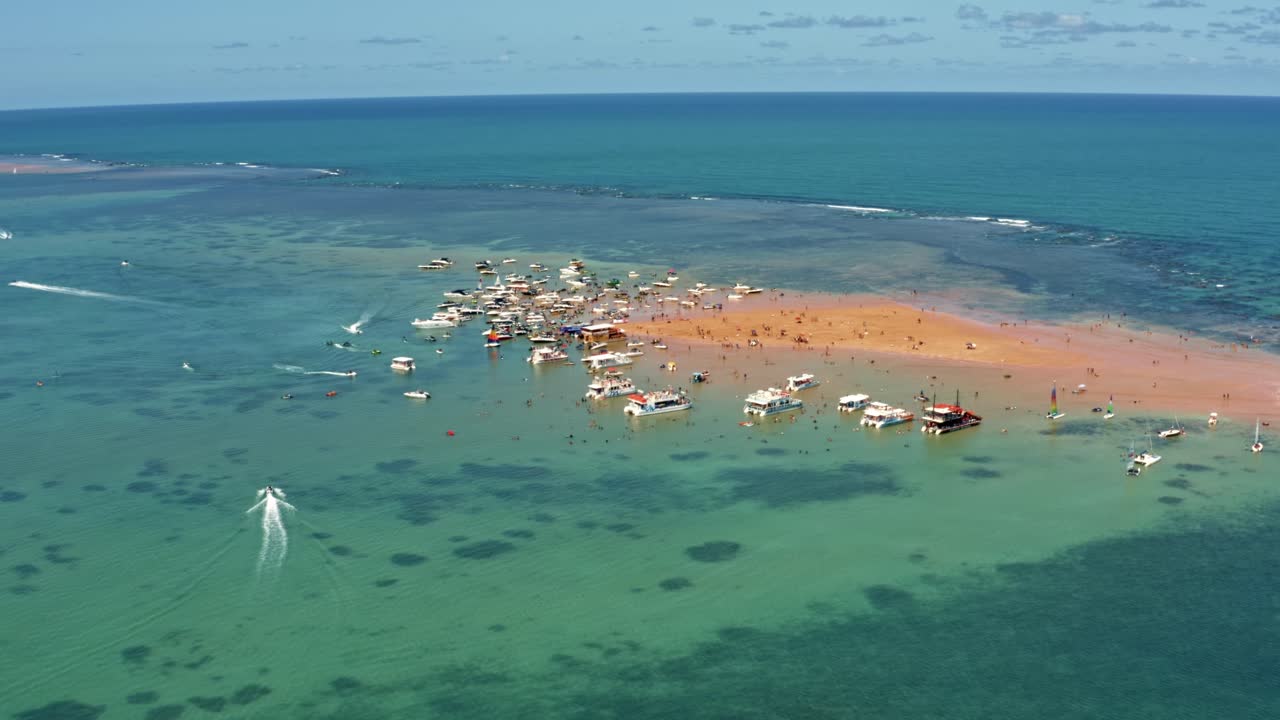 toma aérea derecha de camiones que revela la isla de arena roja en la capital tropical joao pessoa, paraiba, brasil con docenas de barcos turísticos atracados y gente disfrutando del océano en un cálido día de verano