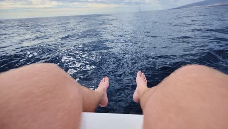low angle pov of man’s legs as yacht moves steadily across open atlantic waters
