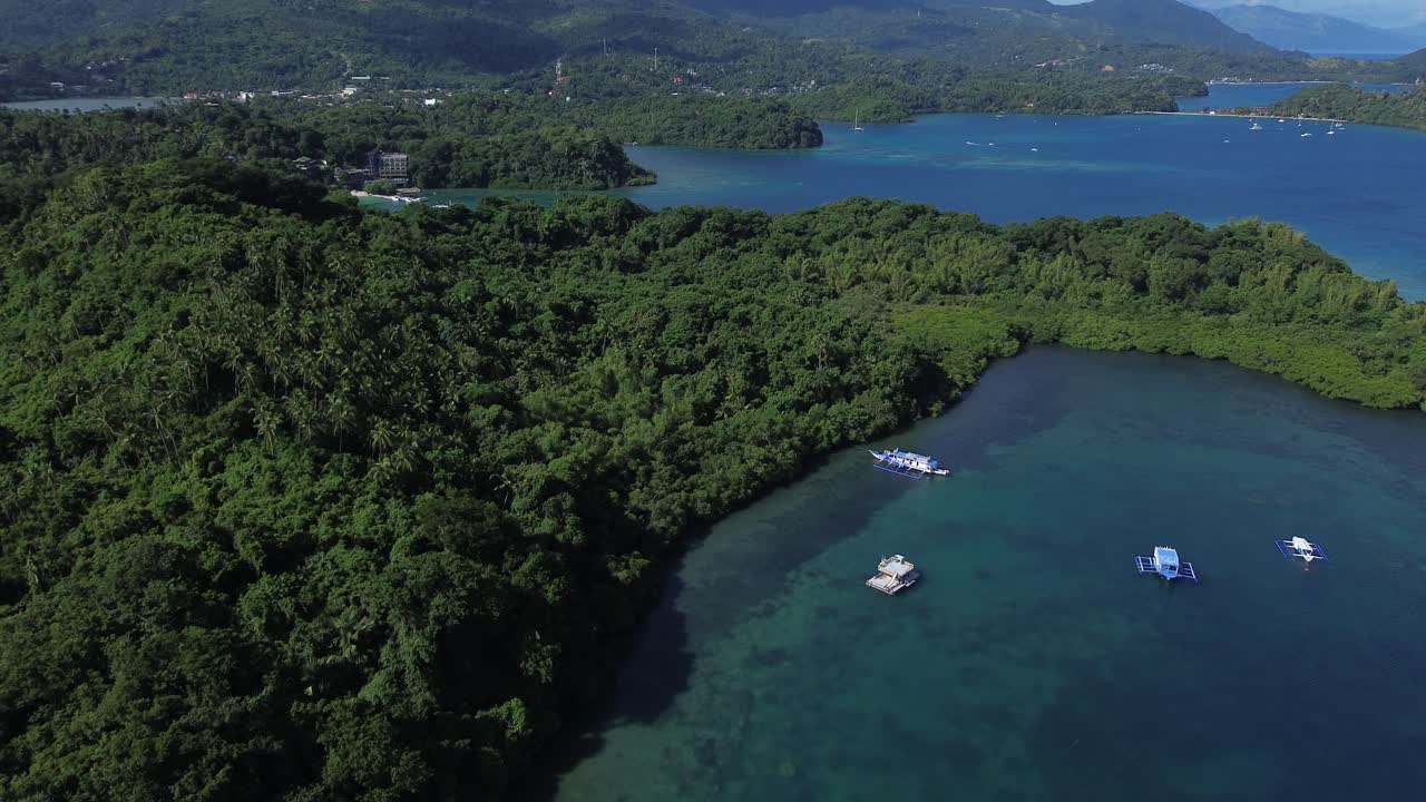 Filmato aereo con drone di una baia tropicale a Puerto Galera, nelle Filippine, con isole verdeggianti e montagne boscose sullo sfondo, acque blu calme e barche ancorate in un sereno paesaggio naturale