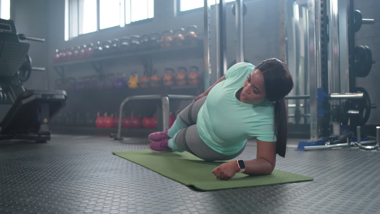 African American mid adult woman starting left forearm plank rolling prone toning core on gym mat