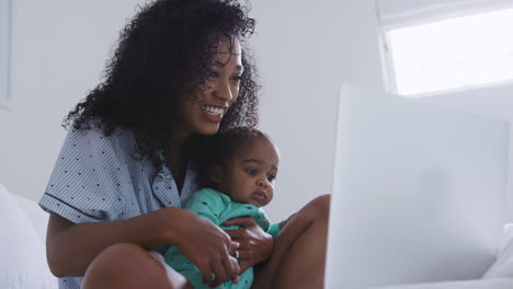 Mutter-Im-Pyjama-Kuschelt-Ihren-Kleinen-Sohn-Im-Schlafzimmer,-Während-Sie-Von-Zu-Hause-Aus-Am-Laptop-Arbeitet