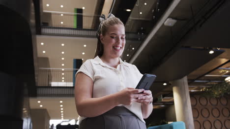 using smartphone, businesswoman smiling and checking messages in modern office