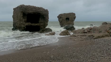 grandes olas tormentosas rompiendo contra las ruinas abandonadas del edificio de fortificación junto al mar en los fuertes del norte de karosta en liepaja, costa del mar báltico, salpicadura de olas, día nublado, plano medio