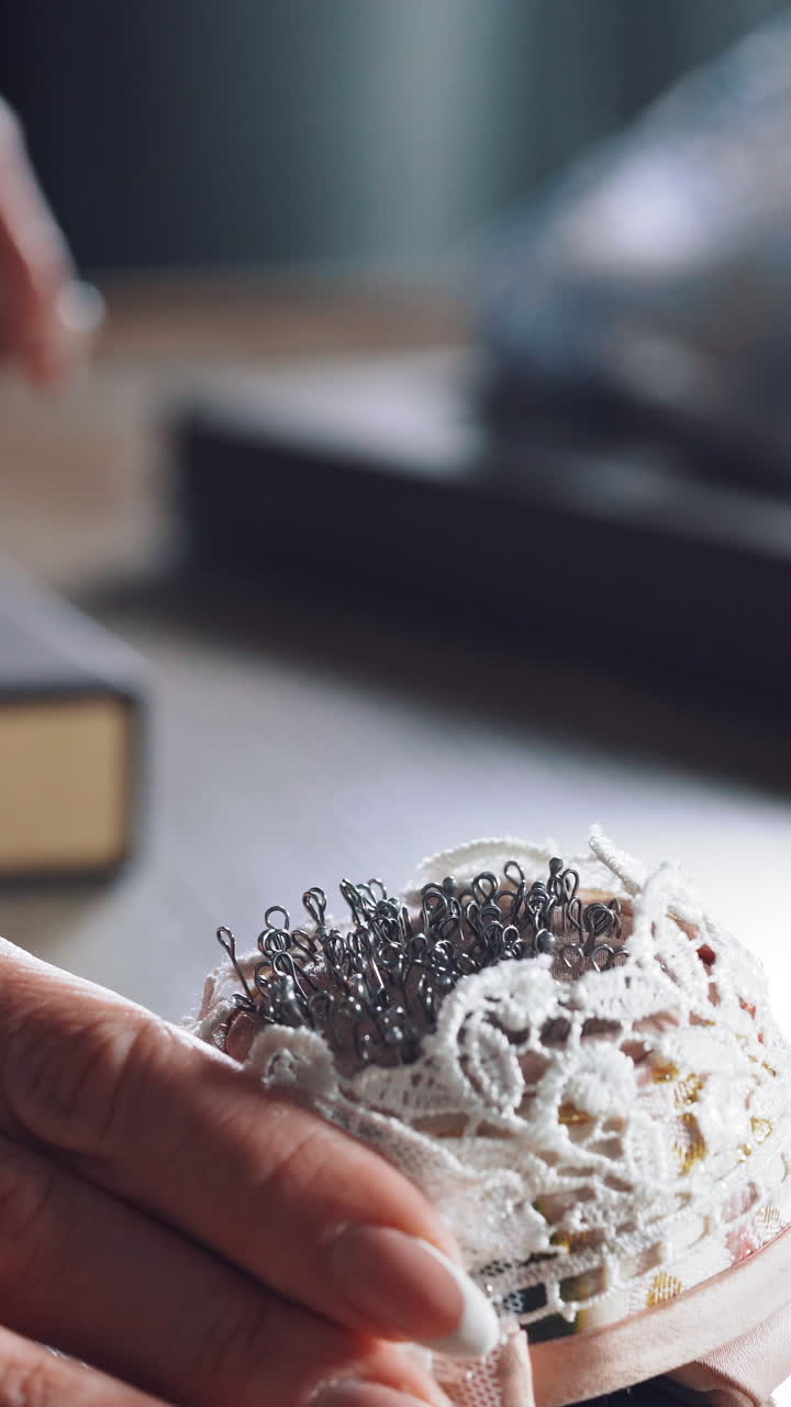 Young tailor is taking spoos from the beautiful pincushion. Many black sewing pins in a small white pillow for seamstress on the wooden table. Vertical video