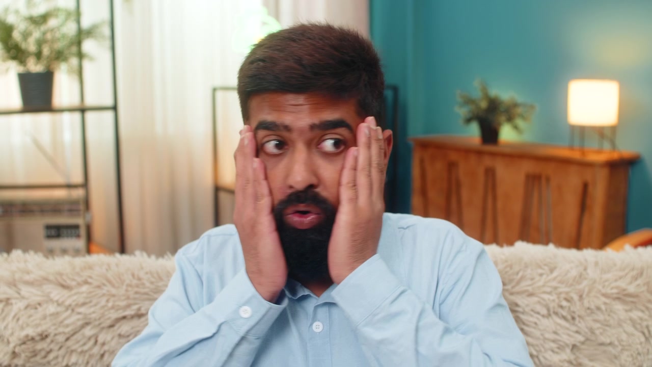 Indisk mand holder sig til hovedet med opspilede øjne i panik overvældet af stressreaktioner og voldsomt pres indendørs