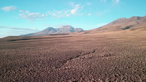 Drohne-Fliegt-über-Die-Chilenische-Wüste-Mit-Einem-Vulkan-Im-Hintergrund-Und-Einer-Lama-Herde-Auf-Dem-Boden