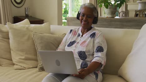 Mujer-Mayor-Afroamericana-Con-Auriculares-Sonriendo-Mientras-Hace-Una-Videollamada-En-Una-Computadora-Portátil-En-Casa