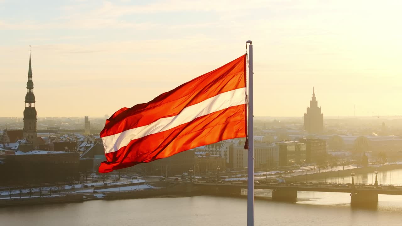 Slow motion drone view of red-white flag waving in Riga’s frosty golden dawn