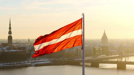 slow motion drone view of red-white flag waving in riga’s frosty golden dawn