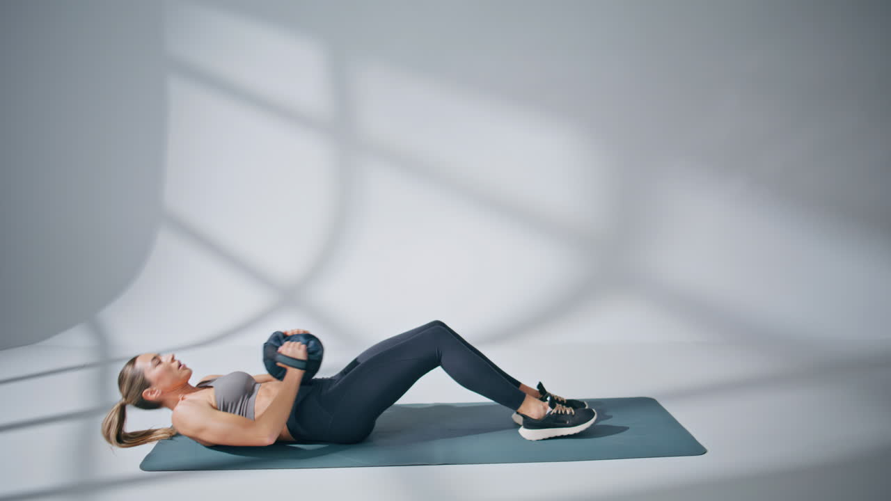 Fit lady training abs holding heavy weight ball indoors. Woman pumping press