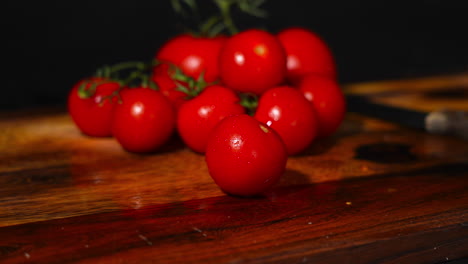 disparo de mano de un tomate cayendo en una tabla de corte de madera con una pila de tomates en el fondo