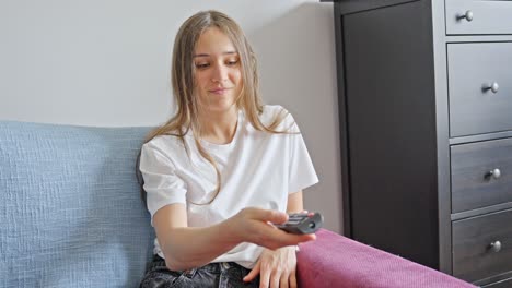 mujer sentada felizmente en el sofá mientras presiona los botones del control remoto hacia la tv en casa, primer plano estático