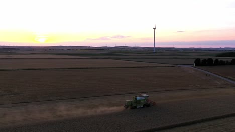 toma aérea en órbita alrededor de la cosechadora industrial durante el trabajo al atardecer en el campo - polvo que se eleva hasta el cielo