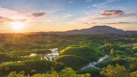drone video capturing green rolling tea hills glowing in sunset light, with reflective water patches between plantations and mountain silhouettes under a golden sky.
