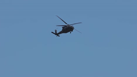 slow motion track shot of flying black military helicopter against blue sky and sunlight