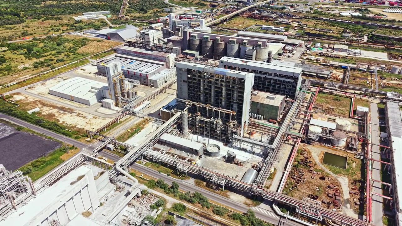Large industrial plant located near a busy highway with multiple buildings and structures on a clear day, showcasing manufacturing processes and equipment in view