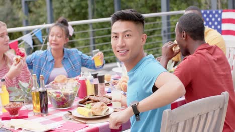 portrait of biracial man sitting at dinner table with diverse friends in garden, slow motion