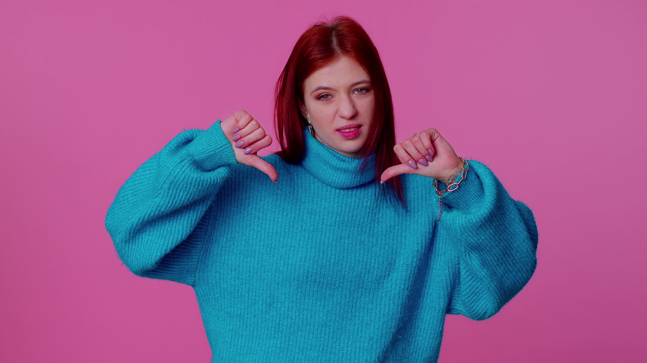 Upset girl in blue sweater showing thumbs down sign gesture, disapproval, dissatisfied, dislike